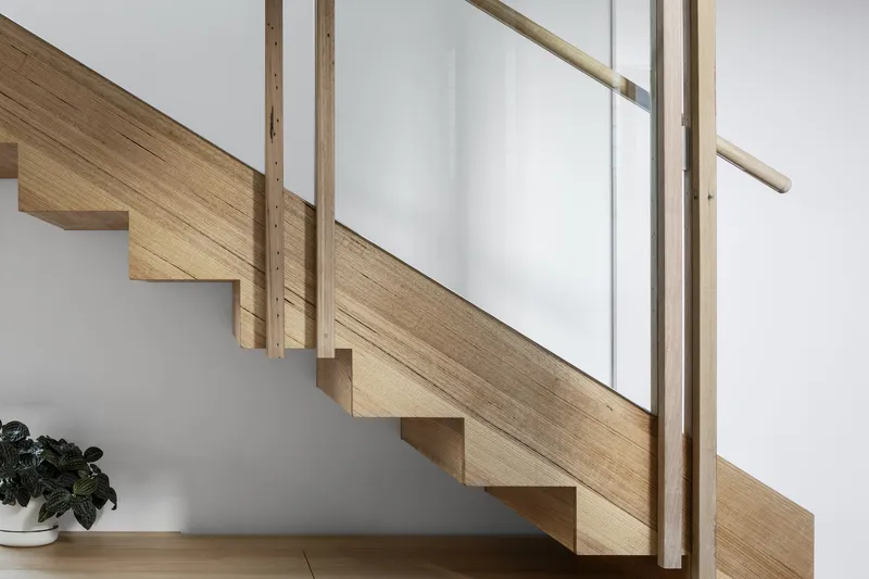 Timber staircase with exposed grain treads and vertical balustrade members against a white wall