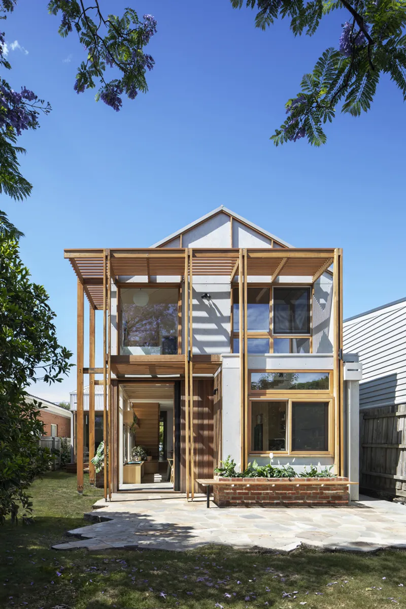 Timber-framed facade with large windows and horizontal louvers framed by overhanging tree branches
