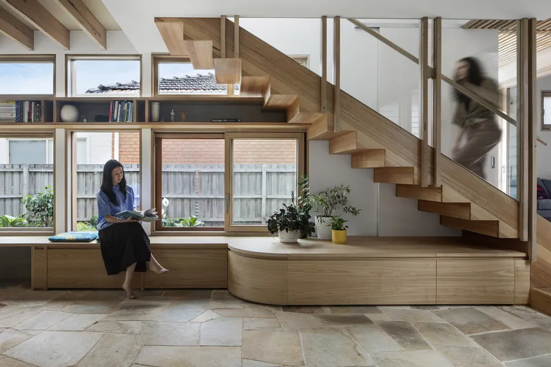 Timber staircase with built-in seating along the window and a person ascending in motion blur