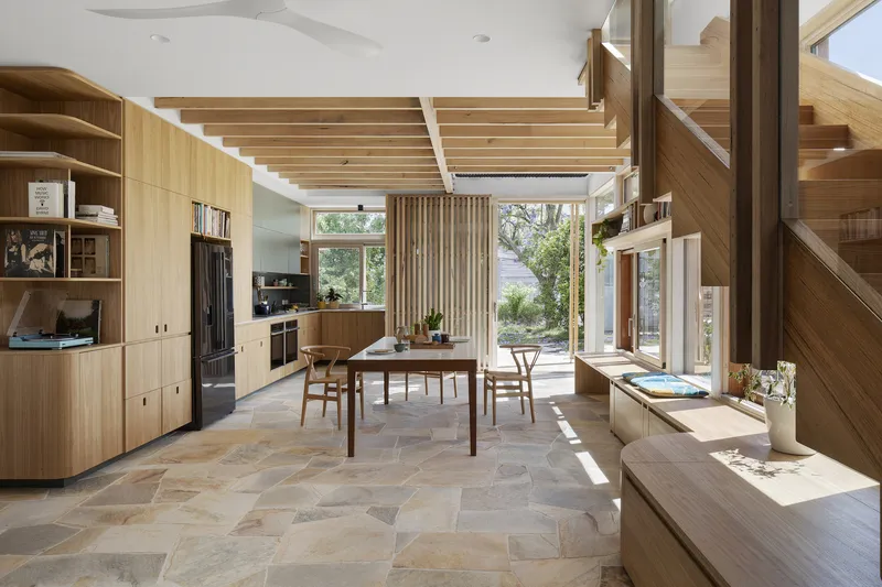 Open-plan dining area with timber slatted ceiling and stone tile flooring bathed in natural light