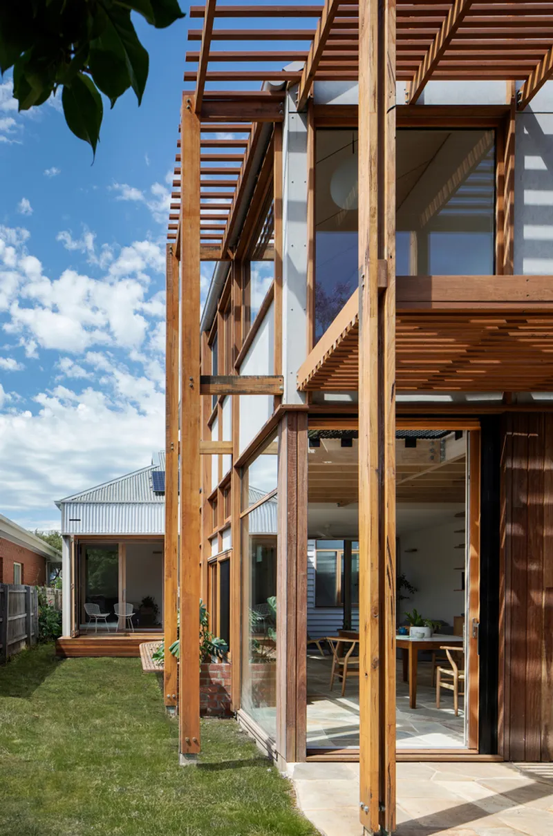 Exterior timber pergola with horizontal slats casting shadows over glazed sliding doors