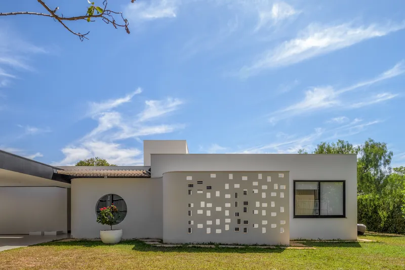 Garden facade with white stucco, scattered square windows, and a circular portal framed by lawn and trees