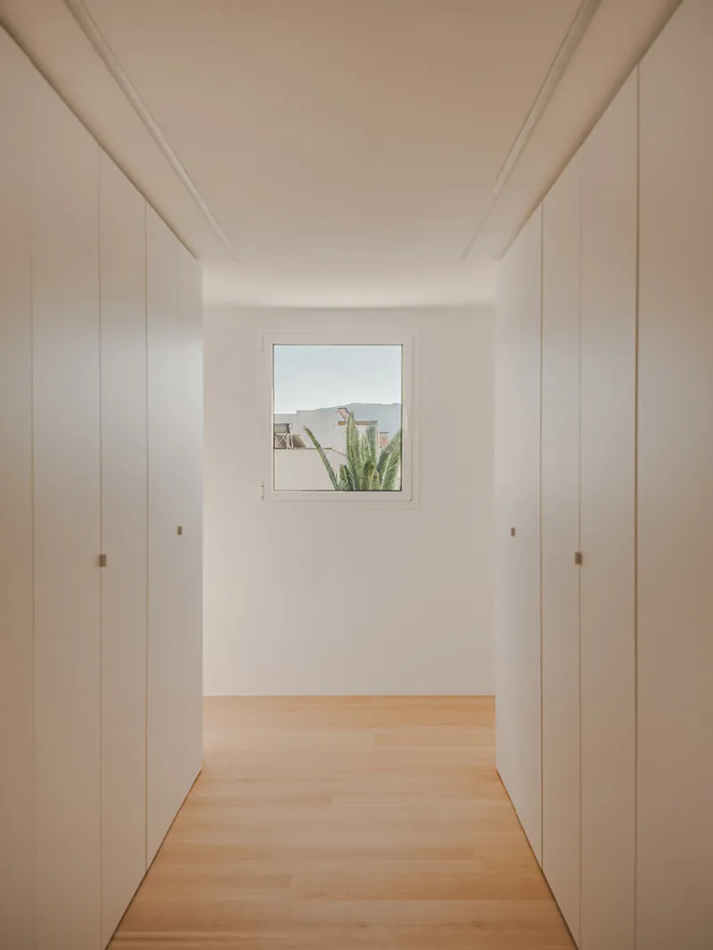 White hallway with floor-to-ceiling closet doors flanking a square window framing palm fronds