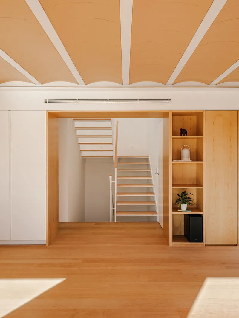 Open-riser timber staircase framed by white cabinetry and built-in shelving under exposed ceiling beams