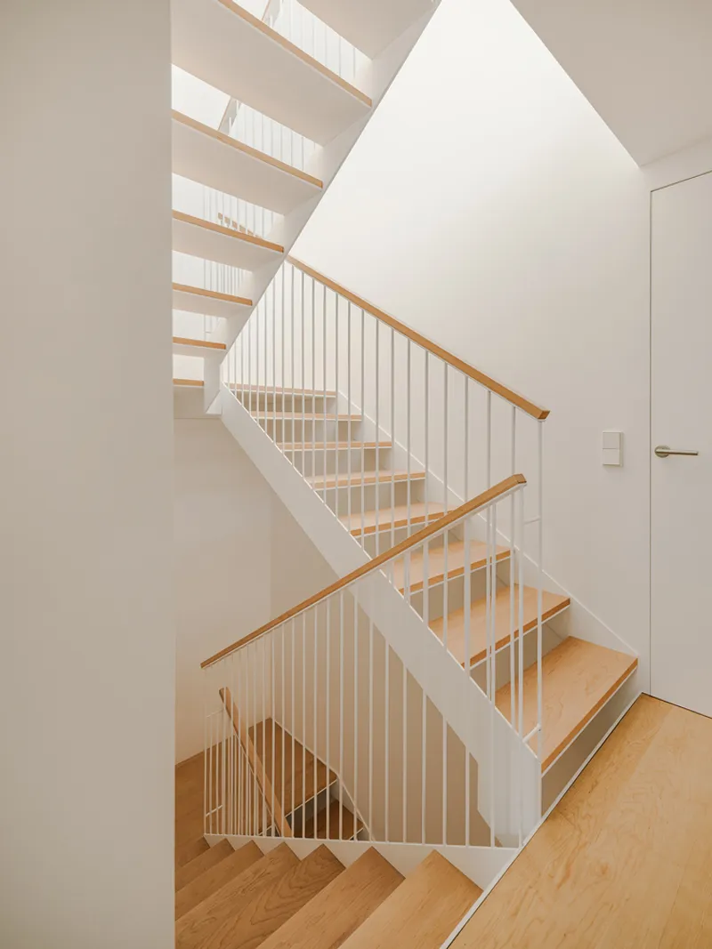 Switchback staircase with white risers, timber treads and vertical rod railings under a skylight