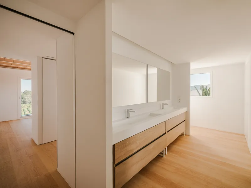 Floating timber vanity with white countertop and twin sinks beneath a frameless wall mirror