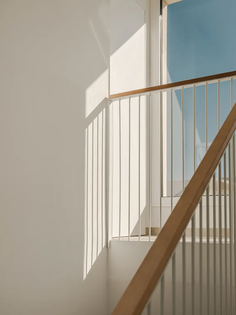 White-painted staircase with timber handrail and vertical balusters in afternoon sunlight