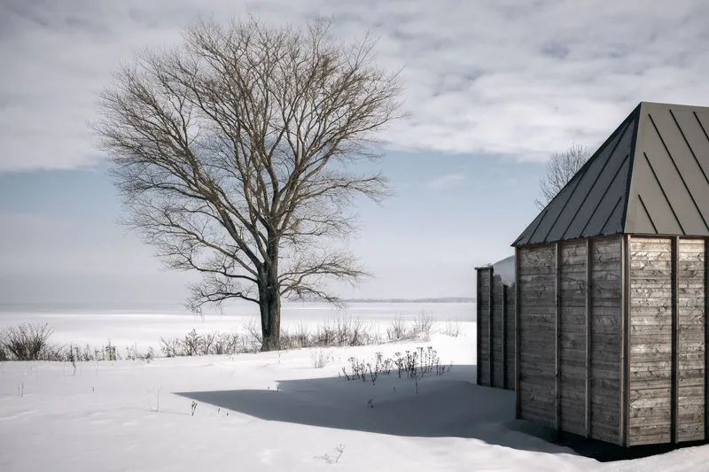 Weathered timber facade with vertical battens and metal roof against a snow-covered field