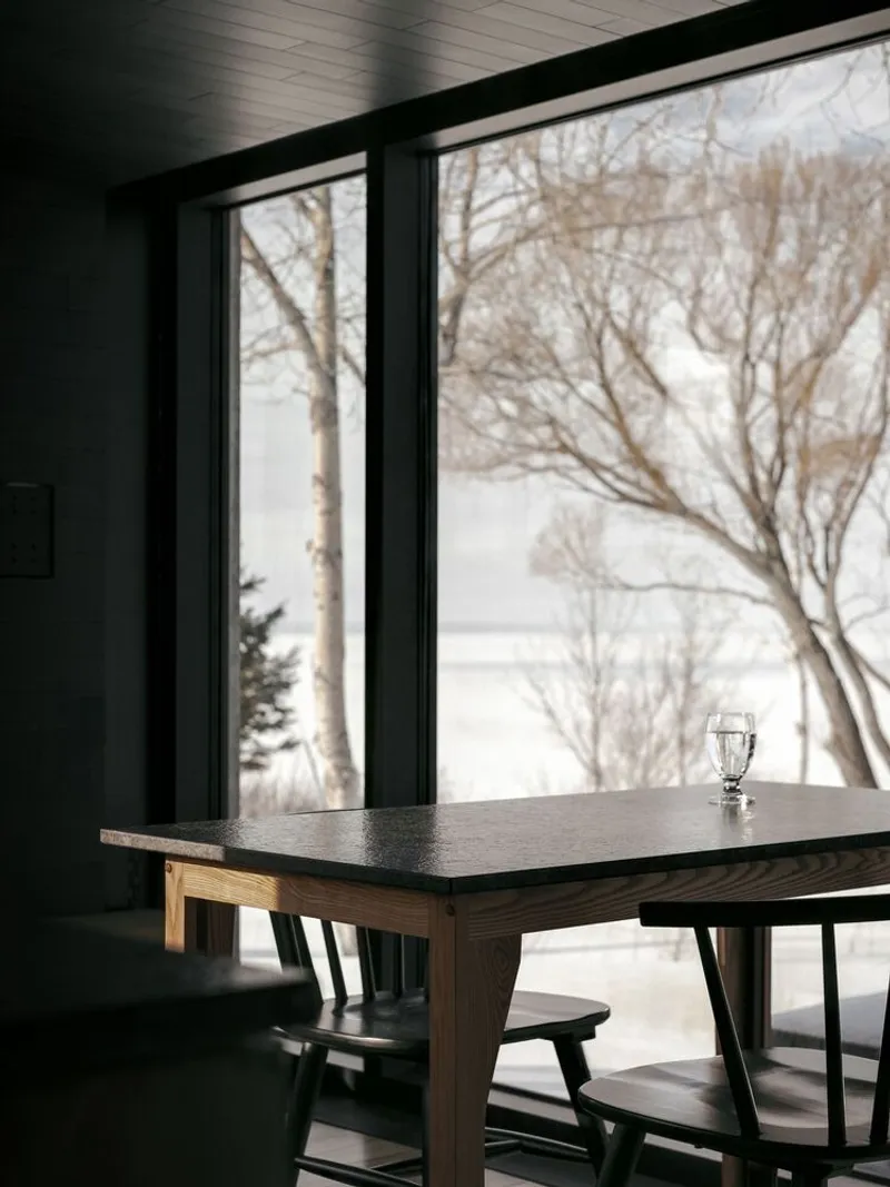 Dark wood dining table and chairs framed by a window overlooking bare winter trees and snow