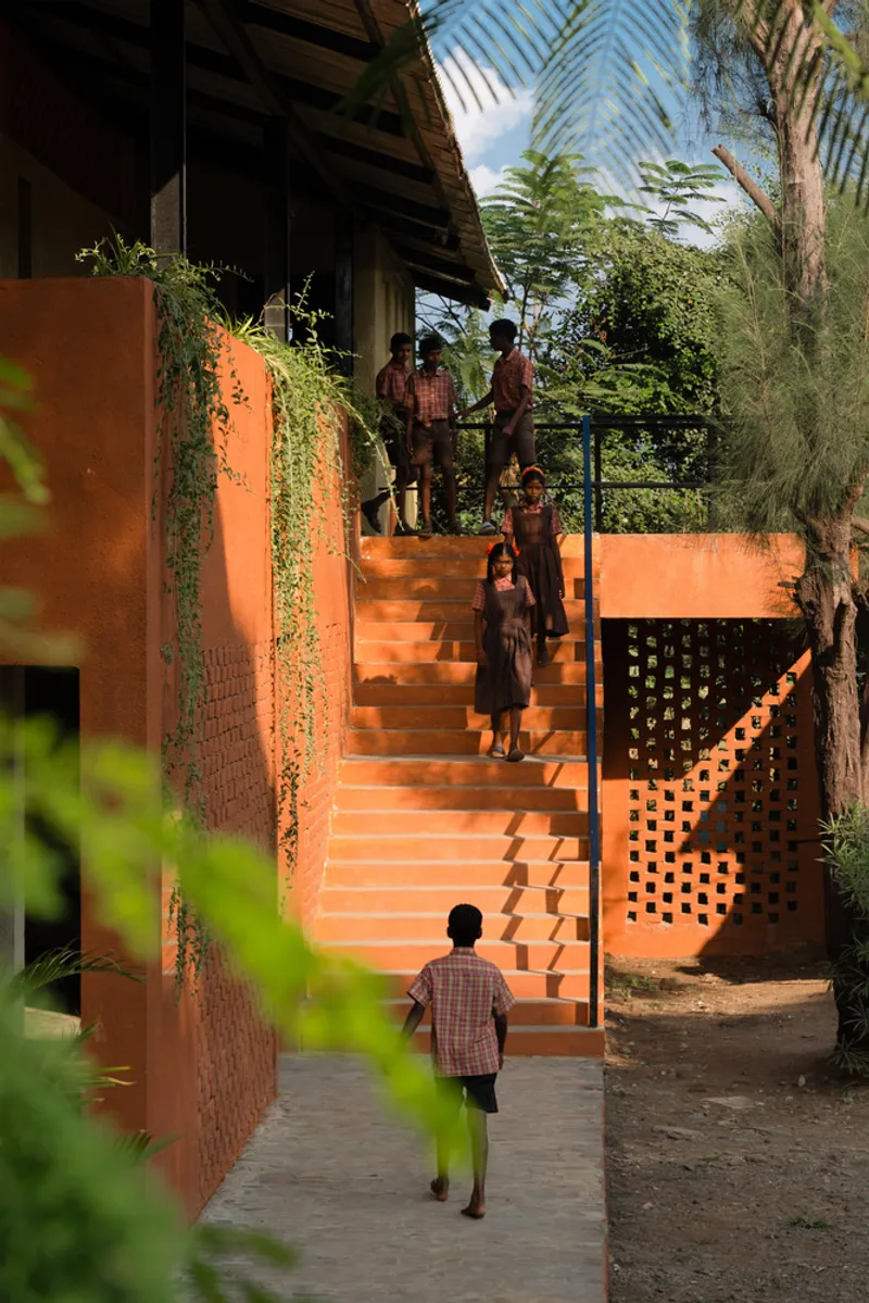 Orange staircase rising between planted walls with trailing vines and children ascending in afternoon light