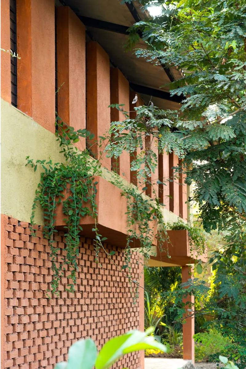 Stacked terracotta brick screen wall below vertical orange fins with vegetation framing the facade