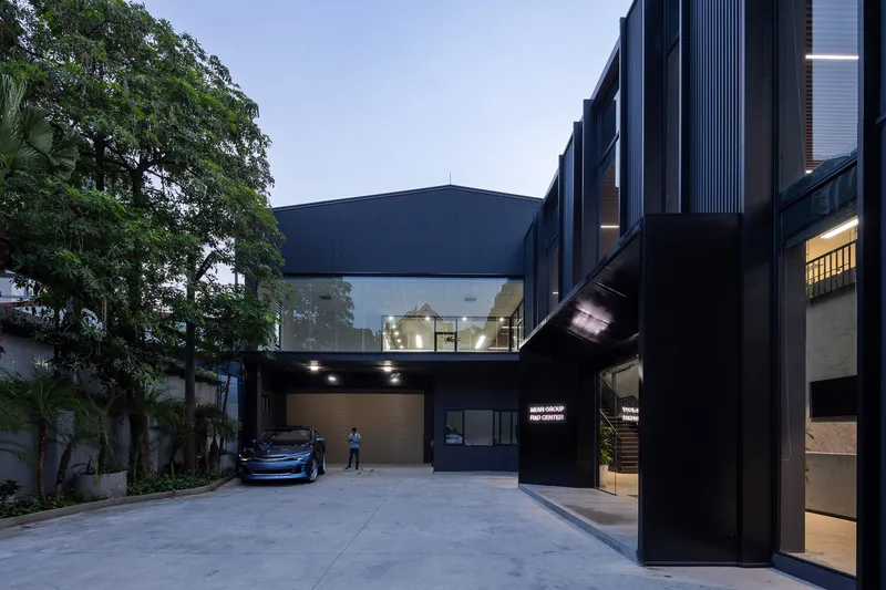 Courtyard entry with dark corrugated metal facade and elevated glass bridge at dusk
