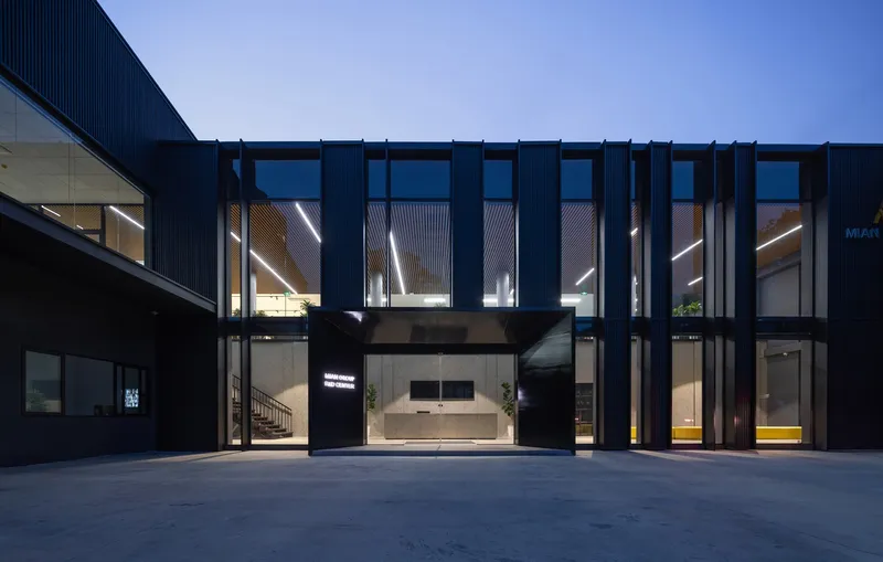 Recessed entrance framed by black vertical fins under corrugated metal overhang at dusk