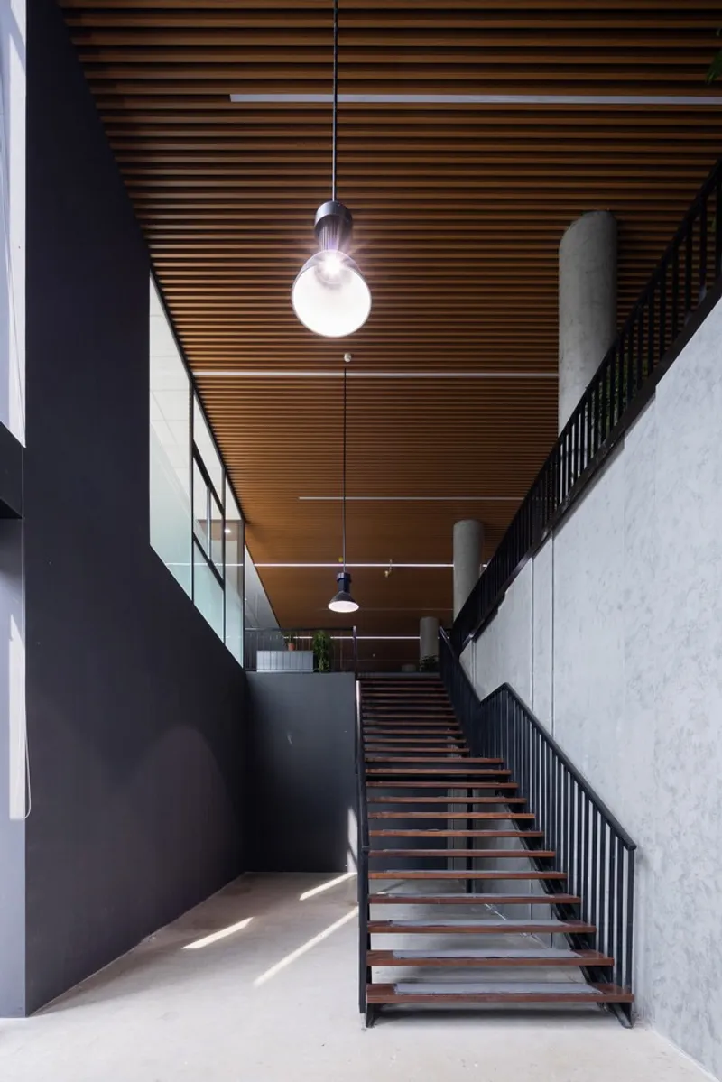 Interior staircase with timber treads and black metal railings beneath a slatted wood ceiling with pendant light