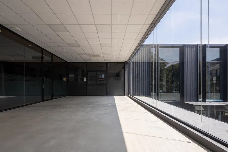 Glazed corridor with white drop ceiling and polished concrete floor opening to a courtyard with corrugated cladding