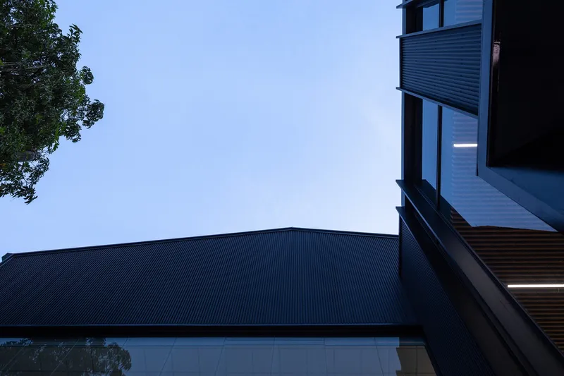 Upward view of corrugated metal canopy against blue evening sky with tree foliage