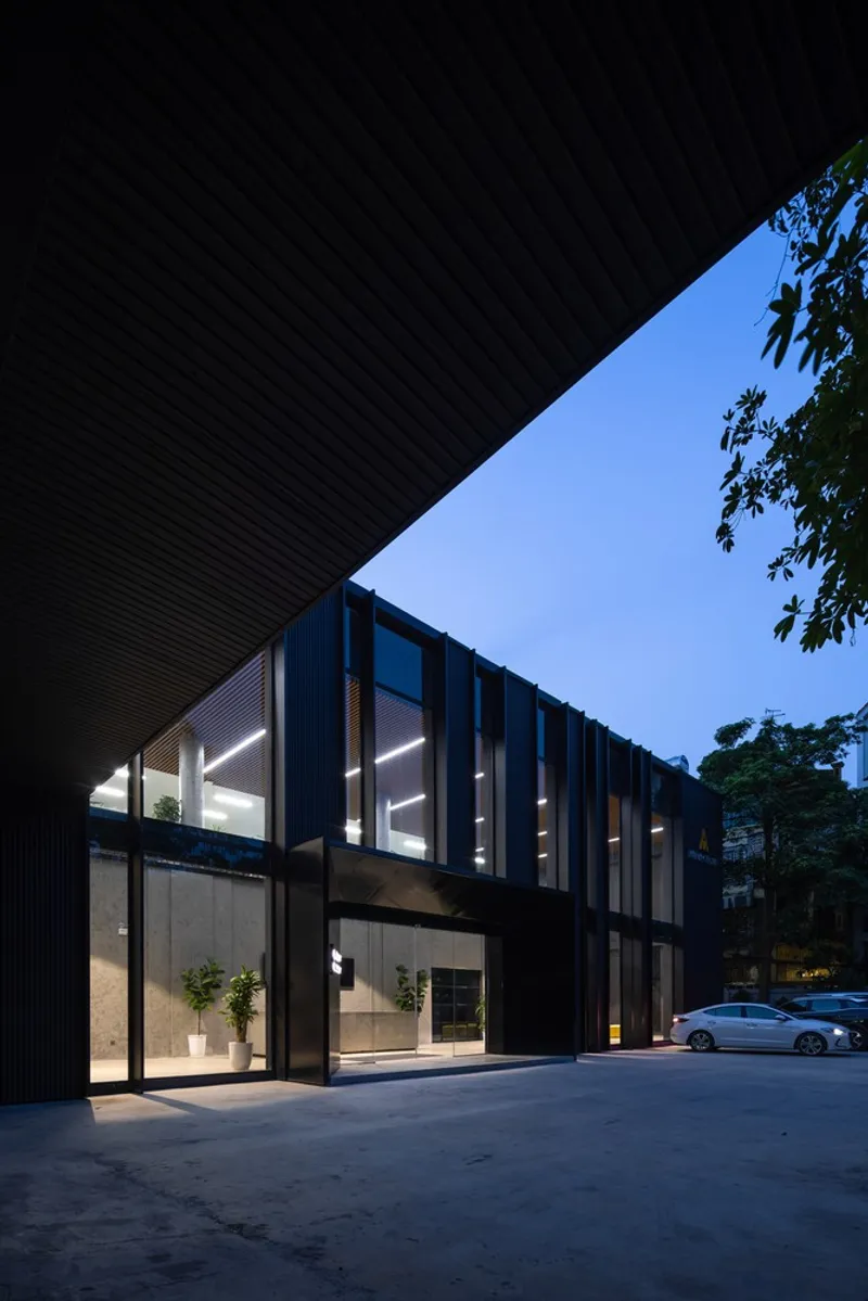 Two-story facade with vertical metal cladding and floor-to-ceiling glazing illuminated at dusk