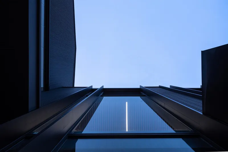 Upward view into a narrow courtyard framed by dark metal cladding and a skylight