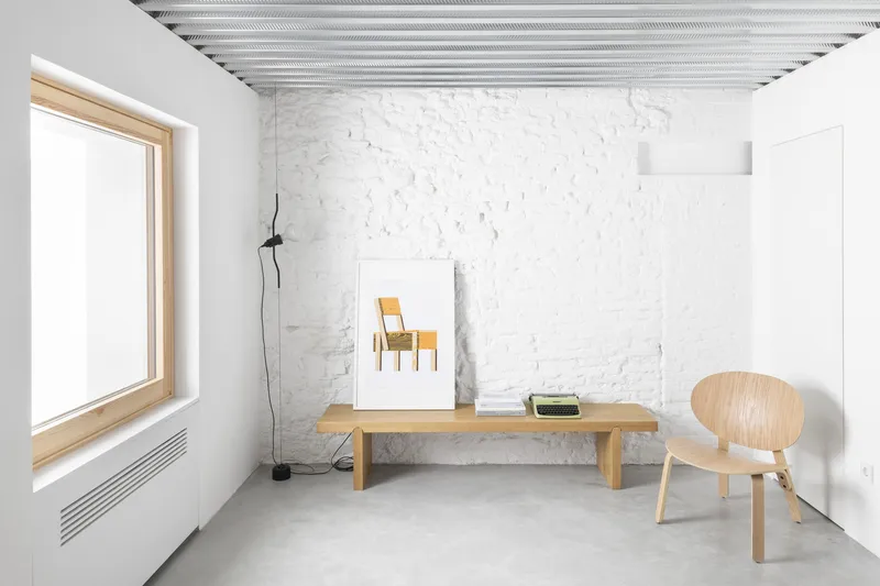 White painted brick wall with timber bench and chair beneath a corrugated metal ceiling in daylight