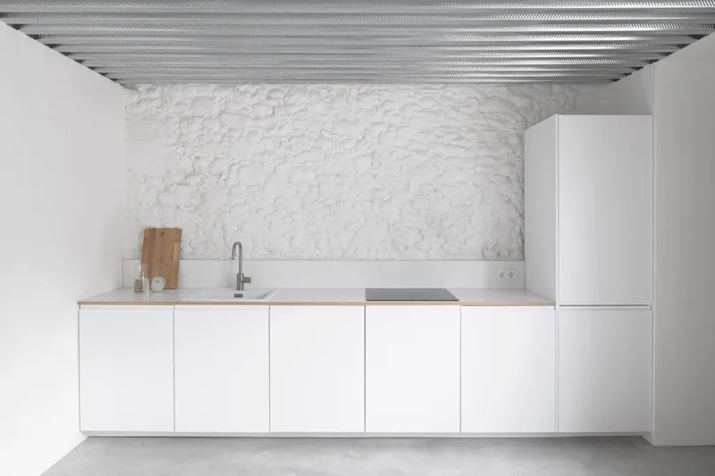White wall-mounted kitchen cabinetry against exposed painted brick with corrugated metal ceiling overhead