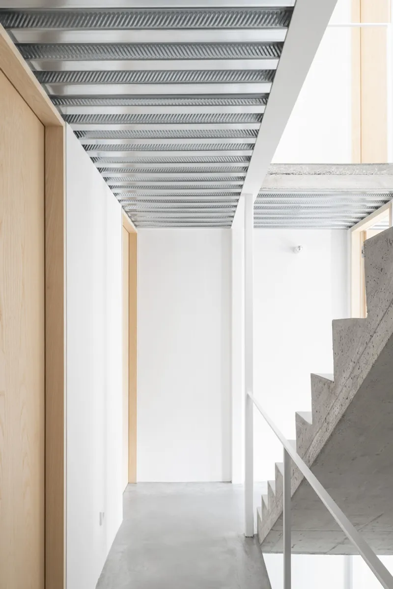 Hallway with concrete stair and light wood doorway under corrugated metal ceiling panels