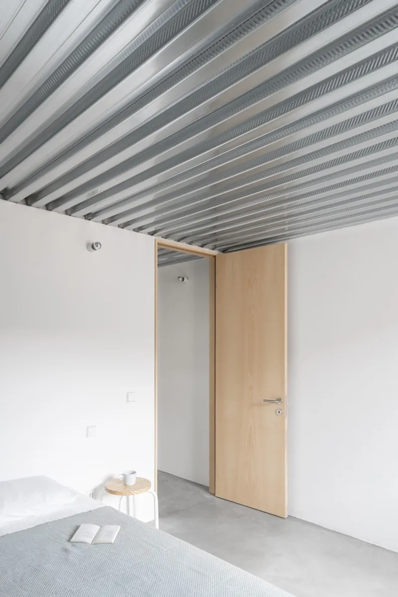 Light wood door opening inward in white room with corrugated metal ceiling