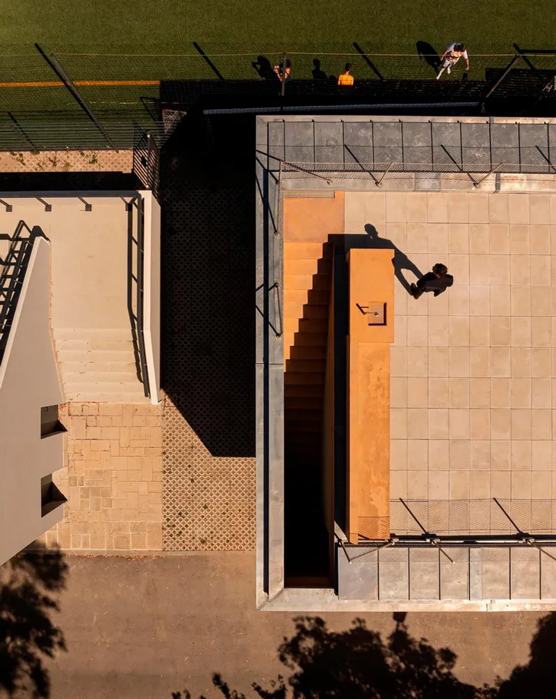 Aerial view of rooftop terraces and courts with athletes casting long afternoon shadows