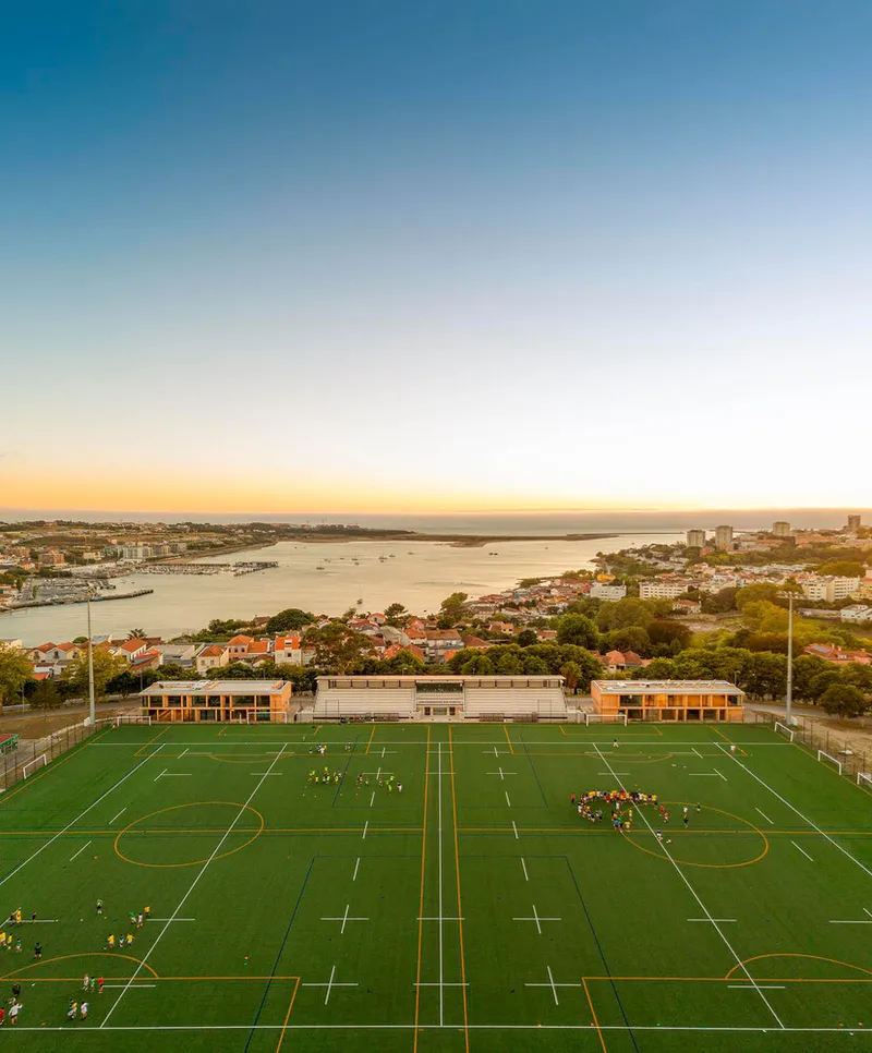Elevated view of playing fields and pavilion buildings overlooking harbor at sunset