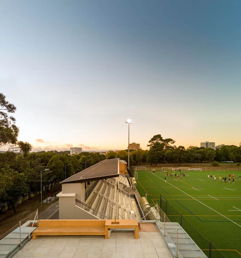 Tiered concrete seating with timber benches overlooking the sports field at sunset
