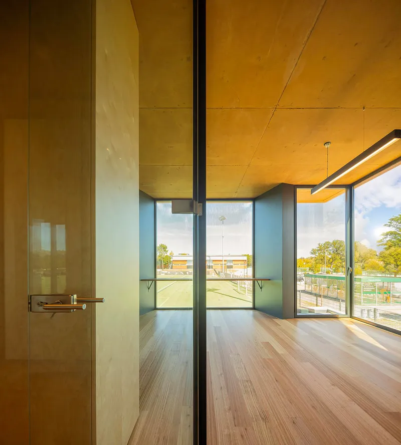 Interior corridor with plywood ceiling and glass doors opening to an exterior playing field