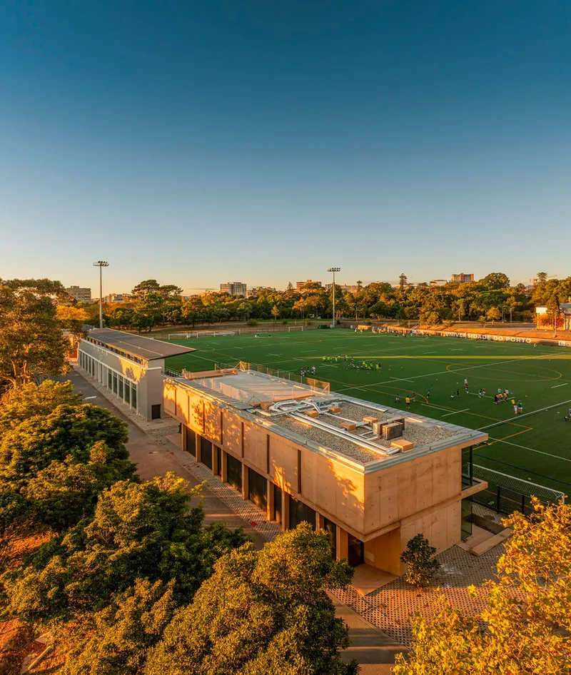 Drone view of the clubhouse with rammed earth facade and rooftop terrace at golden hour
