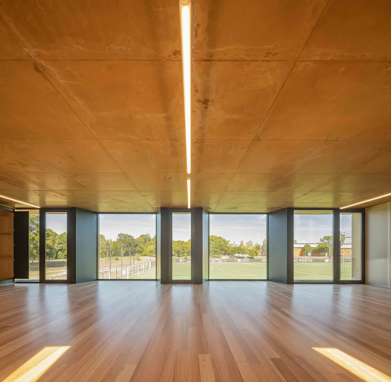 Interior room with timber flooring and ceiling panels framing views of the playing field outside