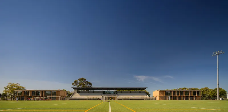 Three pavilions symmetrically arranged across a sports field under a clear blue sky
