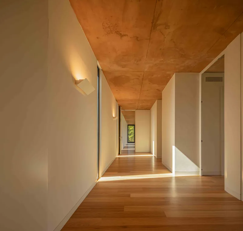 Interior corridor with timber flooring and plywood ceiling leading to distant window framing greenery