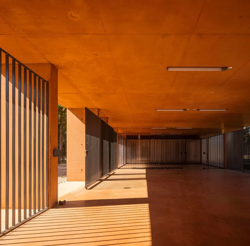 Covered walkway with vertical timber slats and plywood ceiling casting striped shadows on concrete floor