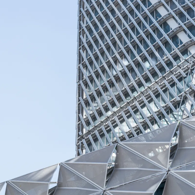Detail of the faceted metal canopy meeting the diagonal lattice facade under clear sky