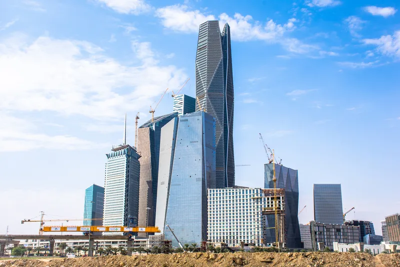 View of the twisted glass tower rising from bare earth with construction cranes nearby