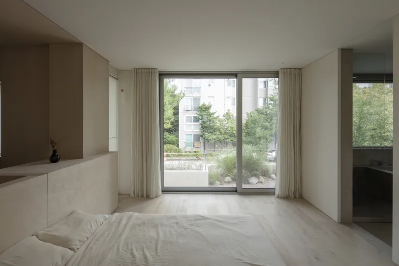 Bedroom with floor-to-ceiling windows opening onto a landscaped terrace with grasses and trees