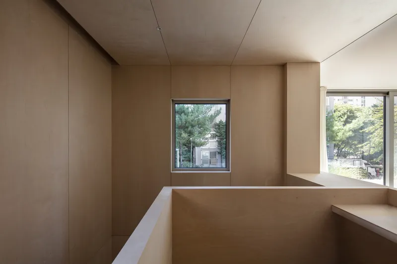 Curved plywood desk built into a corner bay with square window framing street trees