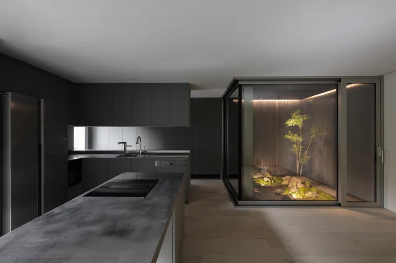 Kitchen with dark concrete island overlooking a glass-enclosed courtyard with bamboo and uplighting