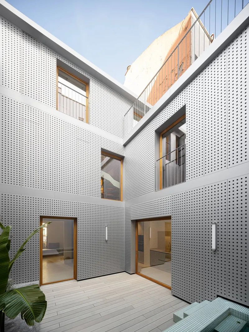 Interior courtyard framed by white perforated metal facades with timber-framed glazed doors