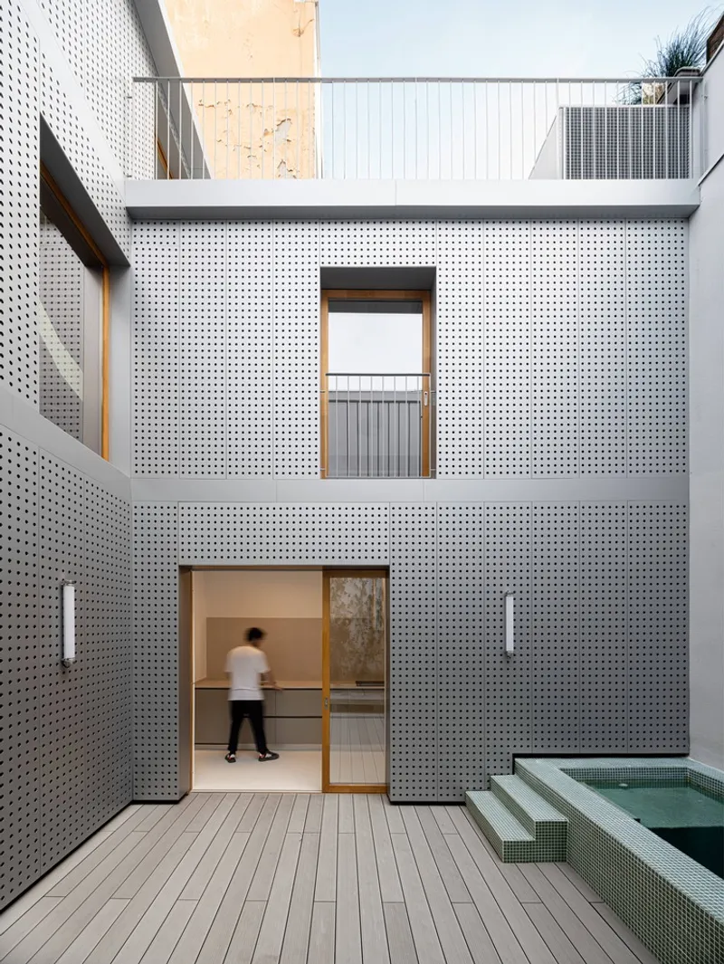 Courtyard facade with perforated metal cladding as a person enters through a timber-framed door