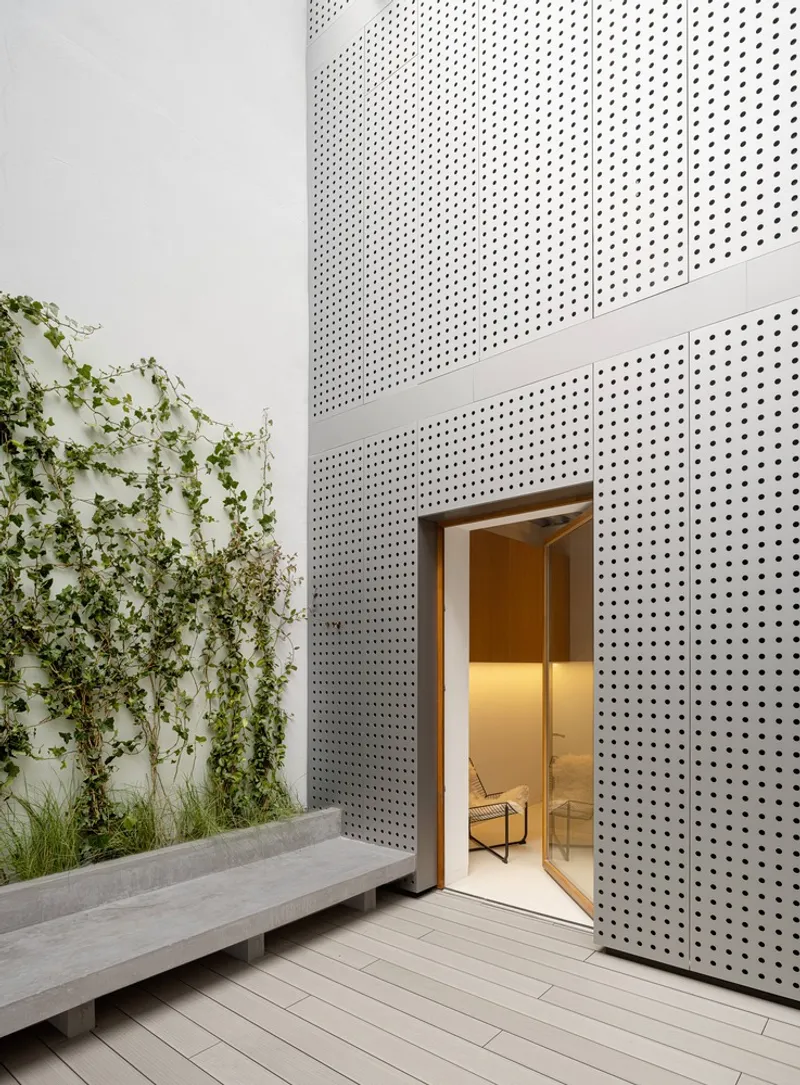 Timber-framed doorway in a perforated metal wall beside a planted bed and concrete bench