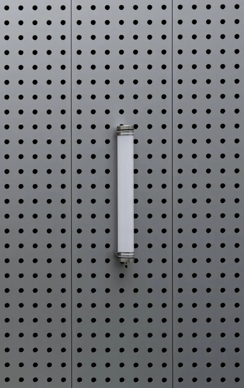 Vertical tubular light fixture mounted on a perforated grey metal panel wall