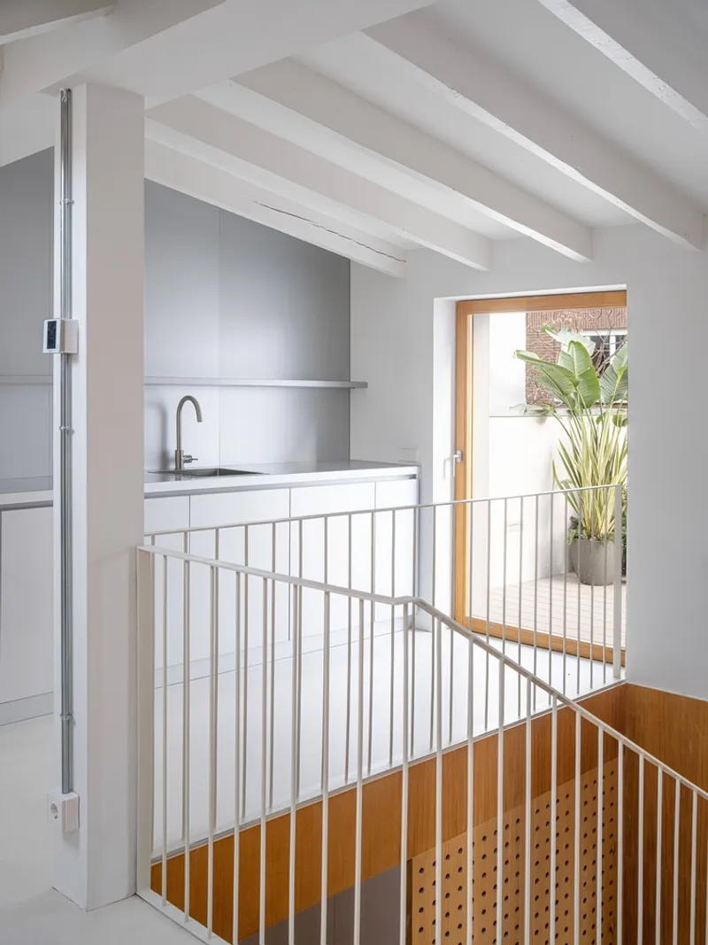 Upper level kitchenette behind white metal railing overlooking stairwell with timber balustrade