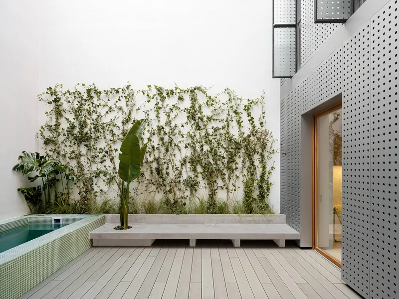 Courtyard with timber deck, concrete planter bench, climbing vines, and perforated metal facade
