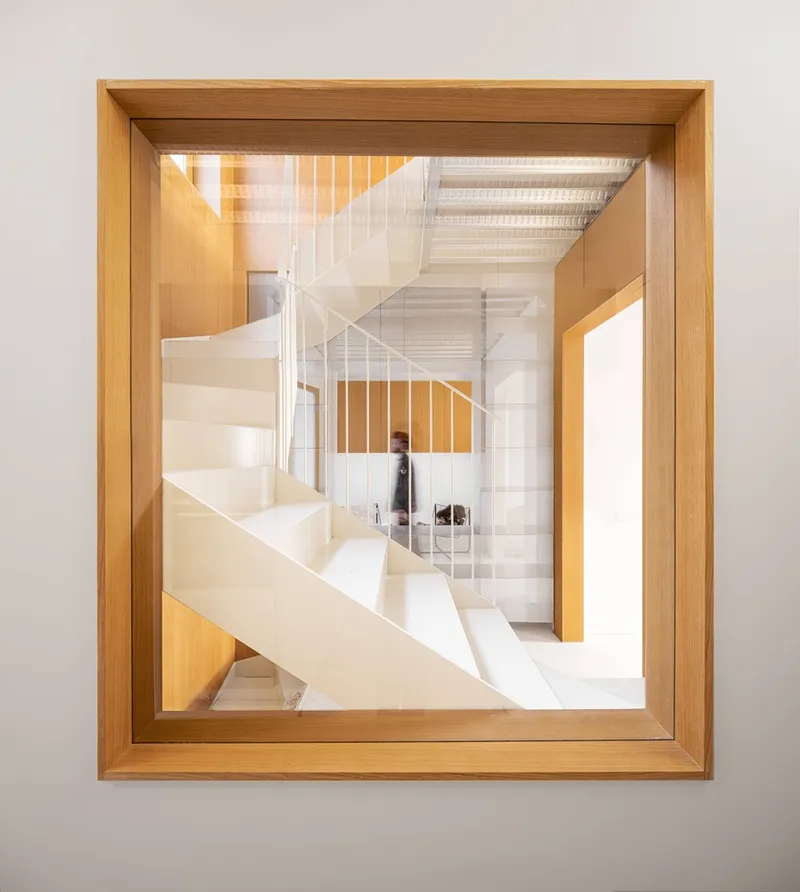 Timber-framed square opening framing a view of the white staircase with a figure in motion