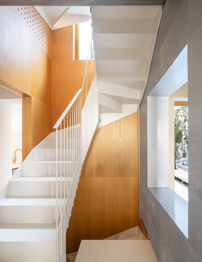Stairwell with white metal railings ascending between timber panels and a grey textured wall
