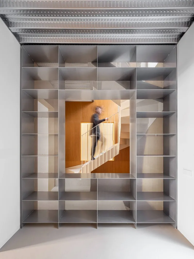 Steel shelving grid with a central opening revealing the timber stairwell and a person ascending