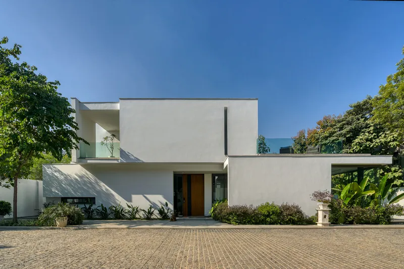Street view of the white stucco entrance facade with recessed carport and brick paved driveway